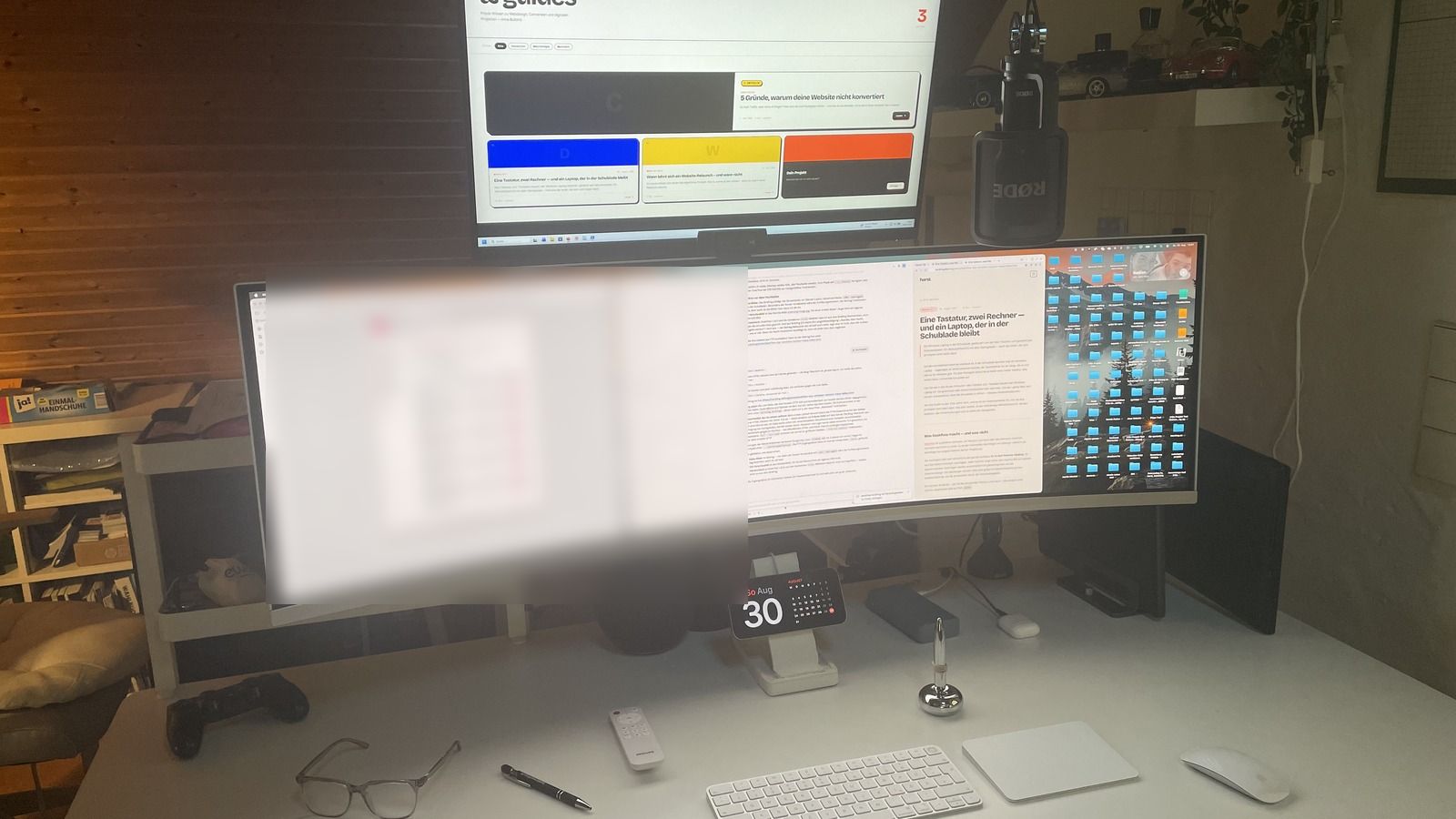 Originalfoto des Schreibtischs: oben ein 27-Zoll-4K-Monitor mit Windows, darunter ein 49-Zoll-Curved-Display mit macOS. Davor liegen eine einzelne Tastatur, ein Trackpad und eine Maus. Ein Fensterbereich auf dem linken Bildschirm ist unkenntlich gemacht.